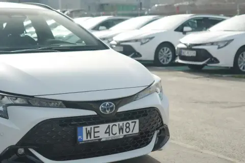 Białe samochody Toyota Corolla, część floty Kinto One, zaparkowane na zewnątrz.