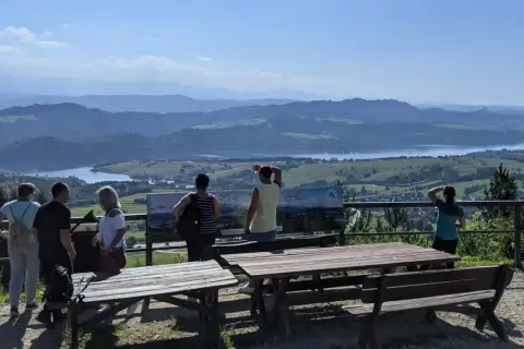Grupa turystów podziwia rozległą panoramę z widokiem na jezioro i góry. Szlak na górę Wdżar oferuje takie widoki.