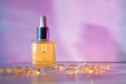 Szklana buteleczka z serum i kapsułki, które mogą zawierać retinol lub retinal, na tle fioletowo-różowego gradientu.