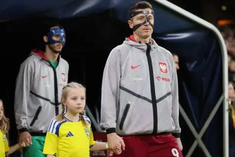 Polscy piłkarze, w tym Robert Lewandowski, wychodzą na murawę z dziećmi. Jeden z zawodników ma niebieską maskę.