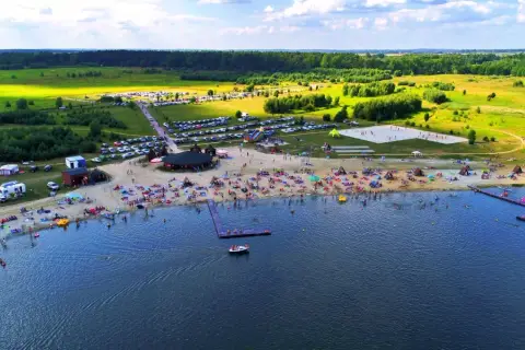 Tętniące życiem jeziora na Dolnym Śląsku latem. Plaża pełna ludzi, namioty, parkingi i zieleń wokół.