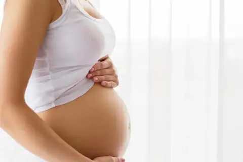Brzuch kobiety w białej koszulce, trzymający go dłońmi. To piękny widok, który przypomina o cudzie życia i przyszłym teście pappa.