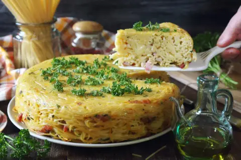 Pyszne spaghetti z piekarnika, zapiekane w formie, z kawałkami boczku i posypane natką pietruszki.