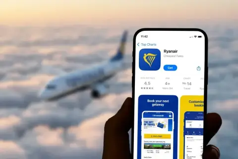 Telefon z aplikacją Ryanair, gotowy do rezerwacji lotu. W tle samolot przelatujący nad chmurami.