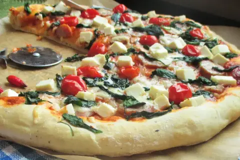 Pyszna pizza ze szpinakiem, pomidorkami koktajlowymi i kostkami sera feta. Idealna na szybki obiad.