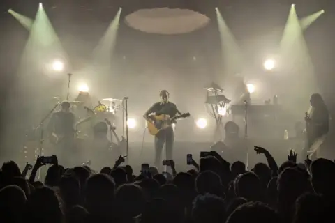 Koncertowy wokalista z gitarą, otoczony dymem i światłami. Publiczność wznosi telefony, wołając "nie zapomnij mnie".