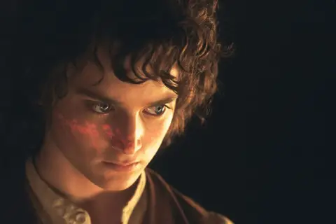 Elijah Wood, kto gra Frodo Bagginsa, z czerwonym znakiem na policzku, w ciemności.