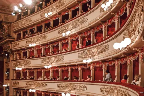 Wnętrze La Scala w Mediolanie, z widownią w lożach, ozdobione złotymi zdobieniami i czerwonymi zasłonami.