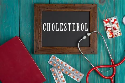 Lekarz bada cholesterol. Na drewnianym tle leżą stetoskop, książka, tabletki i opakowania leków, w tym Lipanthyl.