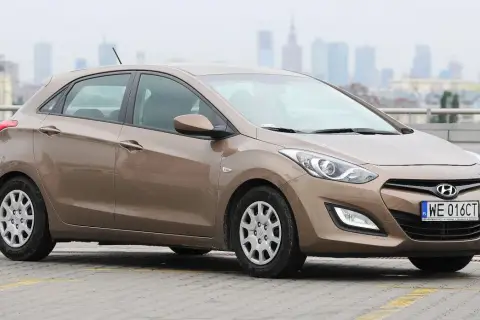 Brązowy Hyundai i30 1.4 benzyna na parkingu, w tle miejska panorama.