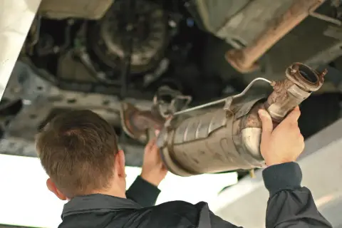 Mechanik trzymający pod samochodem zardzewiały element układu wydechowego, prawdopodobnie DPF.