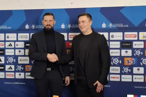 Dwóch mężczyzn w garniturach ściska sobie dłonie na tle ścianki sponsorskiej Rakowa Częstochowa. Zapowiada to nowe, ekscytujące transfery!