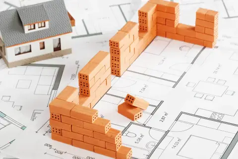 Model domu i mury z cegieł na planie architektonicznym symbolizują początek budowy domu.