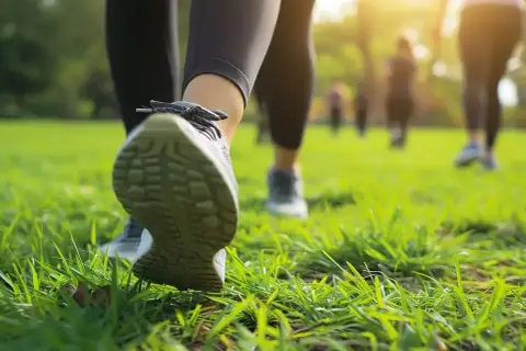 Grupa osób uprawia power walking po zielonej trawie w parku, w promieniach zachodzącego słońca.