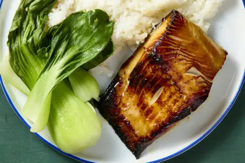 A glistening piece of black cod, marinated and seared to perfection, sits beside fluffy white rice and vibrant green bok choy.