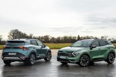 Dwa nowe Kia Sportage GT Line w zielonych odcieniach stoją na mokrej drodze.