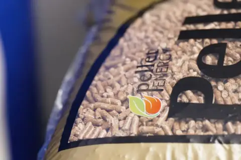 Zbliżenie na worek z pelletem drzewnym. Logo "Pellet Energy" i płomień z liściem. Dowiedz się, jak zrobic pellet.