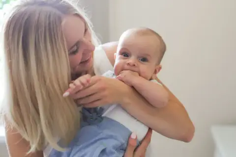 Uśmiechnięta mama tuli dziecko. To piękny widok, jakby właśnie otrzymała becikowe dla kogoś tak cudownego.