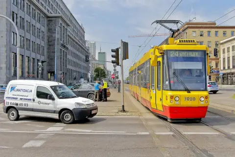 Żółty tramwaj z numerem 24 Gocławek ma pierwszeństwo na skrzyżowaniu, podczas gdy policjanci rozmawiają z kierowcą białego vana.