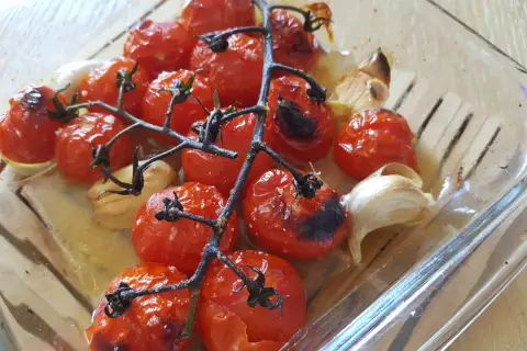 Tomates cerises au four, caramélisées et parfumées à l'ail, dans un plat en verre.
