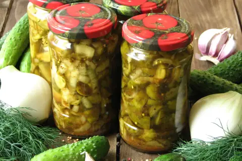 Słoiki z ogórkami w curry ze skórką, otoczone świeżymi ogórkami, cebulą, czosnkiem i koprem.