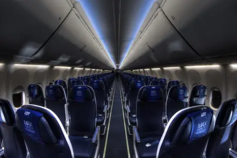 Wnętrze samolotu Boeing 737 MAX 8 LOT, rzędy ciemnych foteli z niebieskimi zagłówkami z logo LOT MAX.