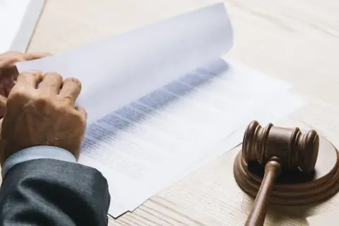 Ręce w garniturze przeglądają dokumenty, obok młotek sędziowski. Może to być akt notarialny gwarantujący dożywotnie zamieszkanie.