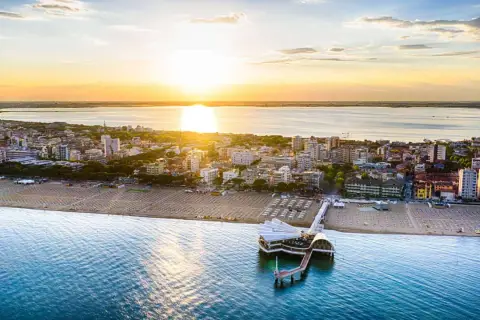 Coucher de soleil sur Lignano, Italie. La plage et la mer s'étendent à perte de vue, avec un pont moderne se jetant dans l'eau.