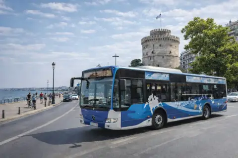 Autobus miejski z motywem fal i mapy Grecji przejeżdża obok Białej Wieży, ikony Salonik.