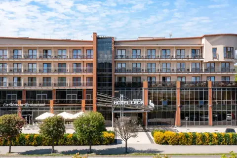 Elegancki hotel Leda Spa z restauracją La Maison, z licznymi balkonami i przeszklonym wejściem, otoczony zielenią.