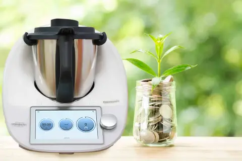 Thermomix i słoik z monetami, symbolizujące oszczędność energii. Dowiedz się, ile prądu pobiera Thermomix, by gotować ekonomicznie.