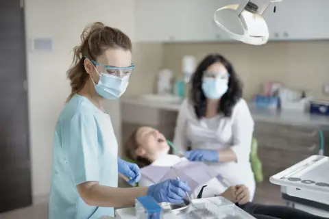 Dentystka w masce i okularach ochronnych wykonuje przegląd stomatologiczny pacjentki.