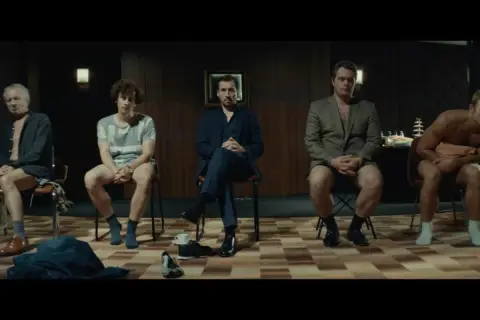 Pięciu mężczyzn siedzi na krzesłach, każdy w innym stroju. Scena z filmu "samiec alfa".