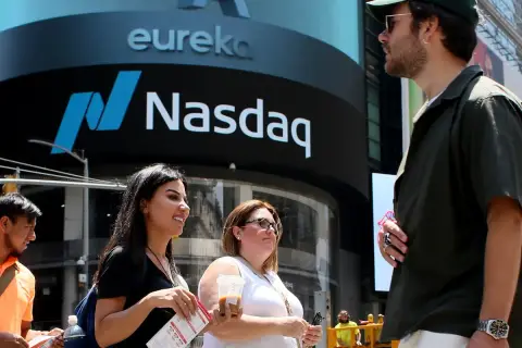 Ludzie przed budynkiem Nasdaq, gdzie handluje się akcjami. Słońce świeci, tworząc cień.