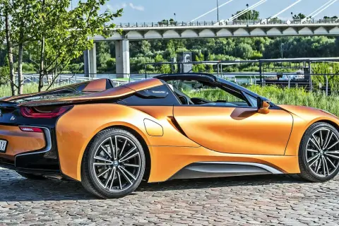 Pomarańczowy BMW i8 Roadster na bruku, pod mostem. Sprawdź aktualną bmw i8 cena.