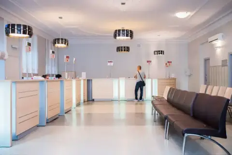 Recepcja w nowoczesnej klinice medycznej z poczekalnią i klientem przy ladzie.