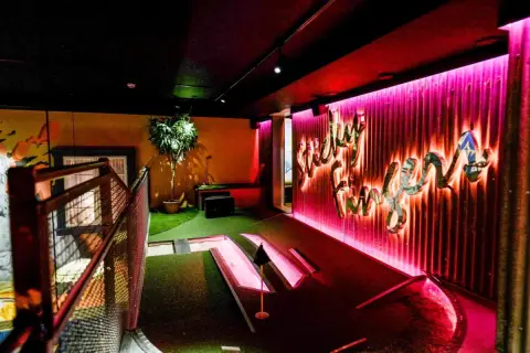 En neonupplyst minigolf bar med en väggtext som säger "Lucky Fun".