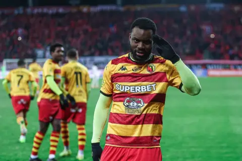 Piłkarz w żółto-czerwonej koszulce pozdrawia kibiców. W tle inni zawodnicy i trybuny. Mecz Widzew Łódź – Jagiellonia Białystok.