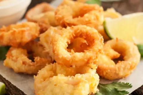 Crujientes calamars a la romana, dorados y listos para disfrutar, acompañados de gajos de limón y perejil fresco.