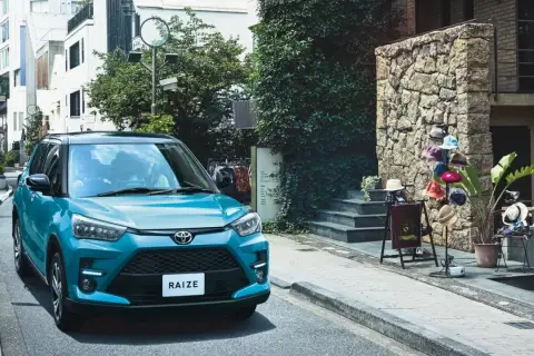 Turkusowy Toyota Raize parkuje na wąskiej uliczce z kamienną ścianą i wystawą kapeluszy.