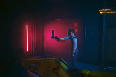W dobra strone cyberpunk. Mężczyzna z pistoletem stoi przed drzwiami, a gracz celuje z żółtej broni.