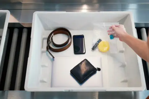 Co wykrywają papierki na lotnisku? Na taśmie leżą: laptop, portfel, telefon, pasek, kosmetyczka z płynami i inne drobiazgi.