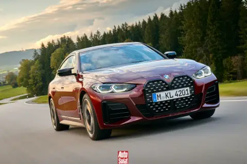 Czerwone BMW G26 z charakterystycznym grillem pędzi po krętej drodze wśród zielonych wzgórz i lasów.