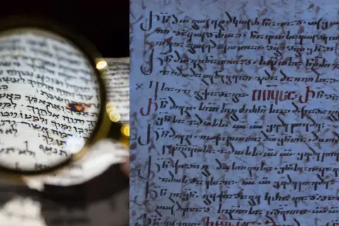 Starożytny manuskrypt z hebrajskimi tekstami, badany przez lupę. Obok fragment starożytnego tekstu w innym języku, być może maur.