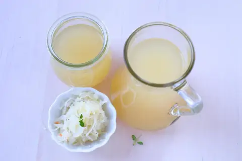 Ein Glas und ein Krug mit Sauerkrautsaft, reich an Vitaminen, stehen neben einer Schale Sauerkraut.