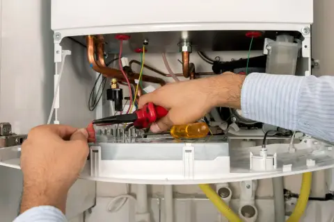 Serwisant De Dietrich naprawia kocioł, pracując przy przewodach i elementach elektronicznych.