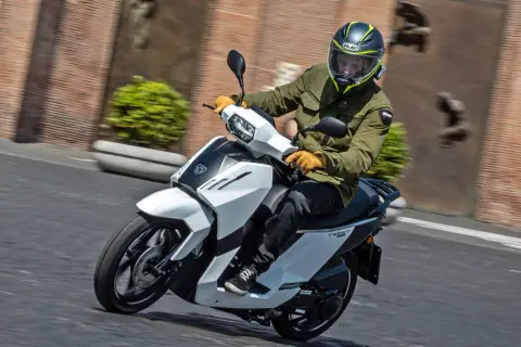 Hombre en scooter Peugeot Tweet 125, con casco y chaqueta verde, circulando por una calle.