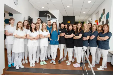 Grupa uśmiechniętych dentystów w białych i granatowych uniformach stoi w gabinecie.