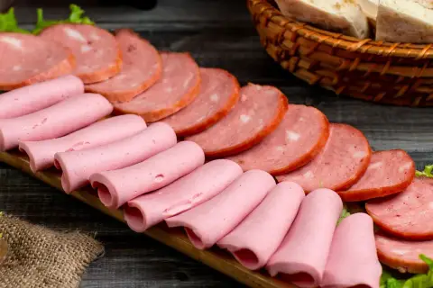 Na desce ułożone są różowe parówki i plastry wędliny. Zastanawiasz się, jakie wędliny są najzdrowsze?