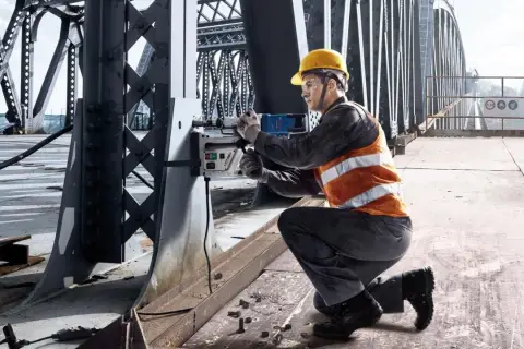 Pracownik na moście używa wiertarki magnetycznej Bosch do prac konstrukcyjnych.
